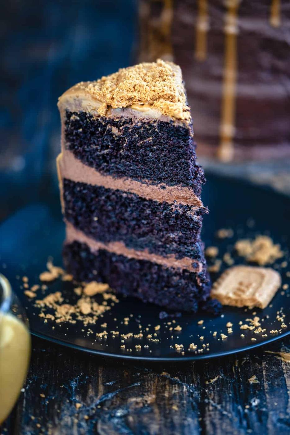 Slice of Biscoff Chocolate Cake on a black plate with Biscoff biscuit crumbs