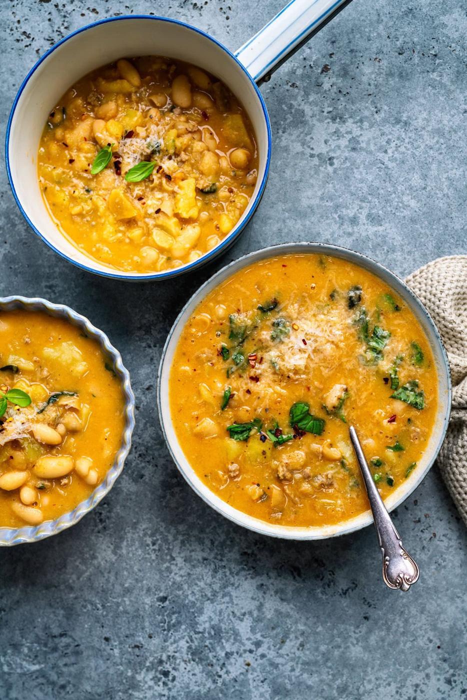 two bowls of white bean and sausage soup with a small pot on the side