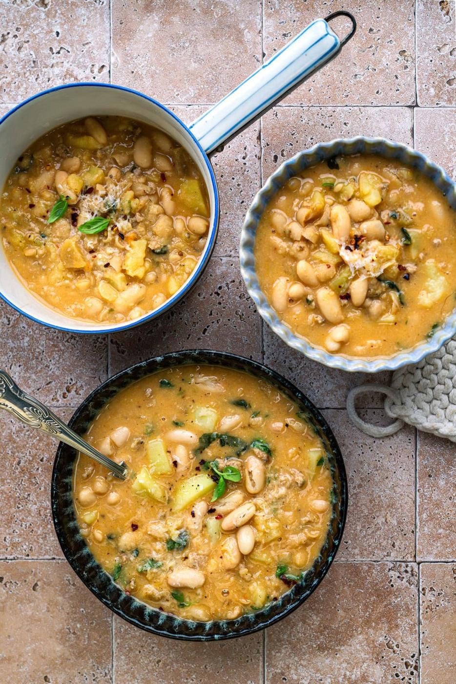 Hearty sausage and cannellini bean soup, two bowls and a pot