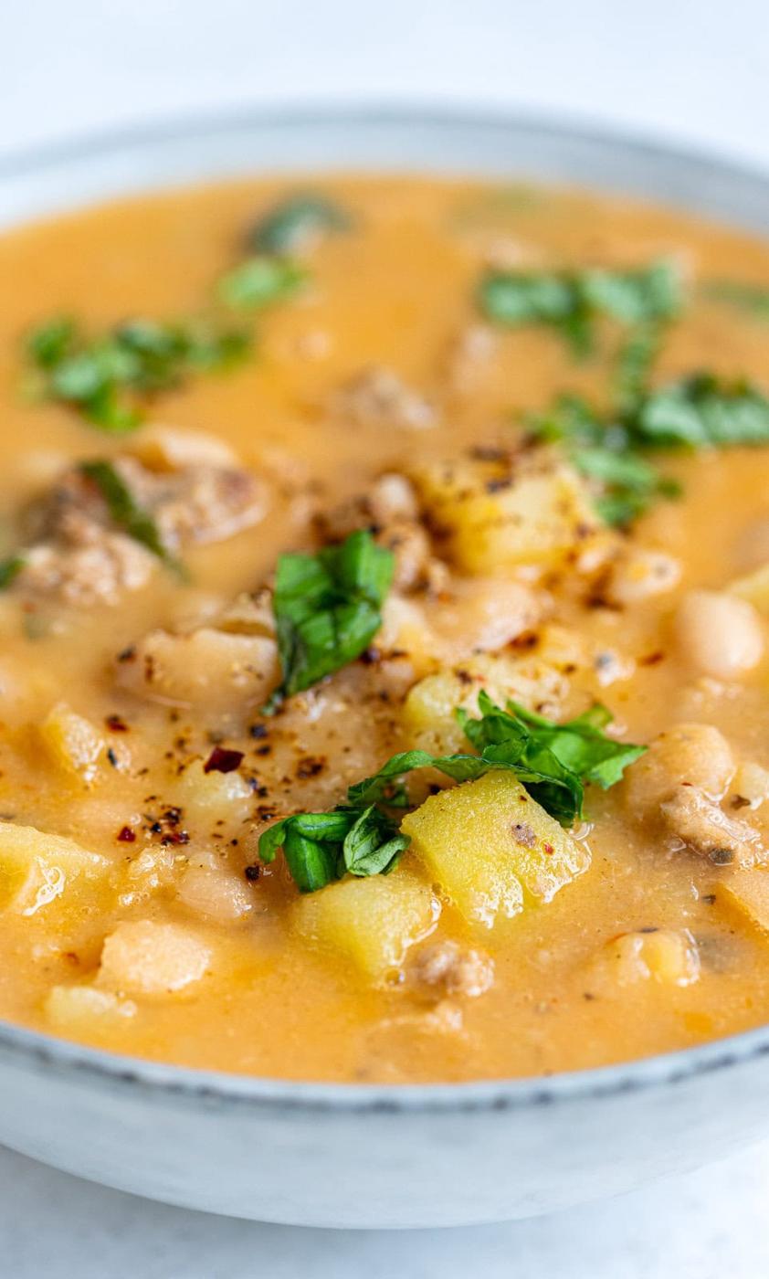 close up on a bowl of bean and sausage soup garnished with fresh basil