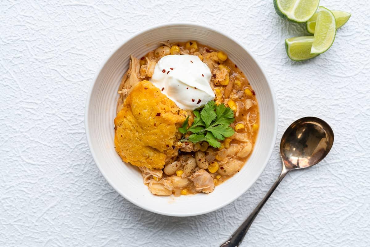 bowl of white chicken chili and cornbread dumpling topped with sour cream and cilantro