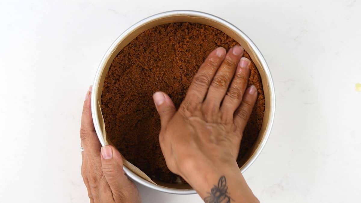 Pressing cookie crumbs into cake pan to make cheesecake base