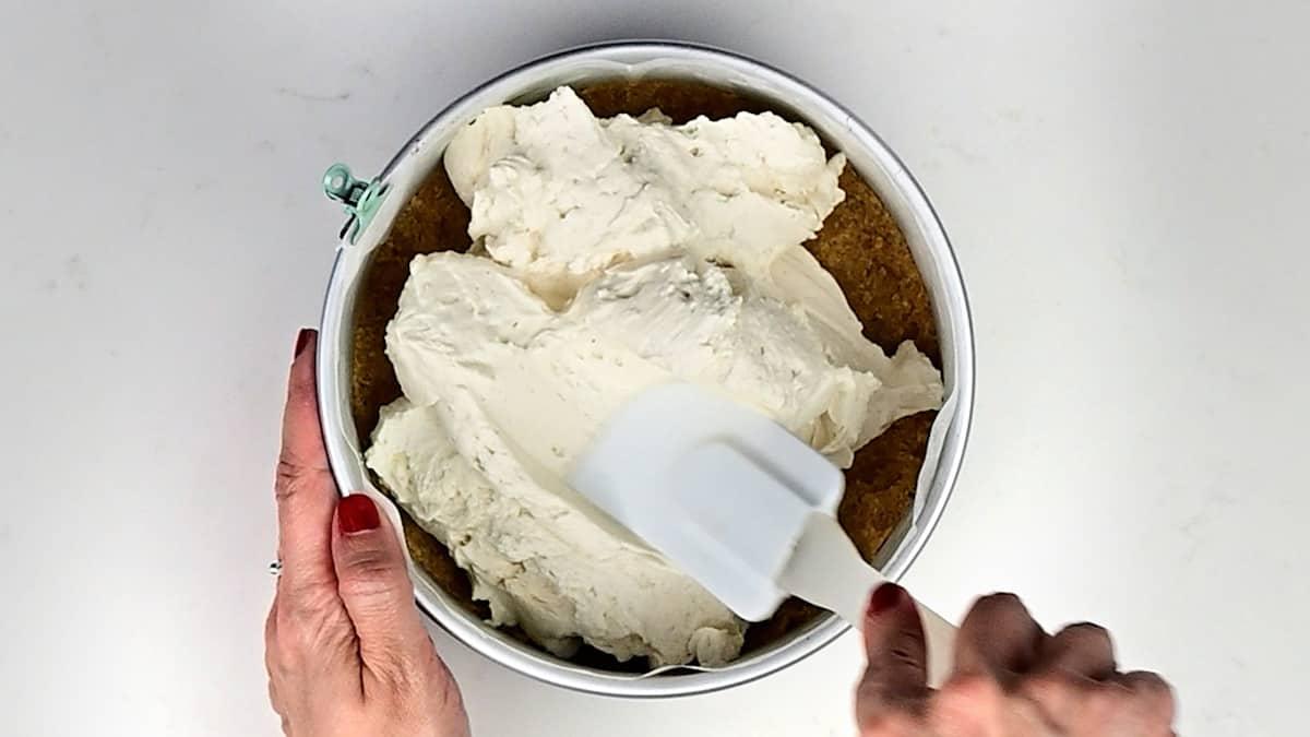 spreading cheesecake filling over base in a cake tin