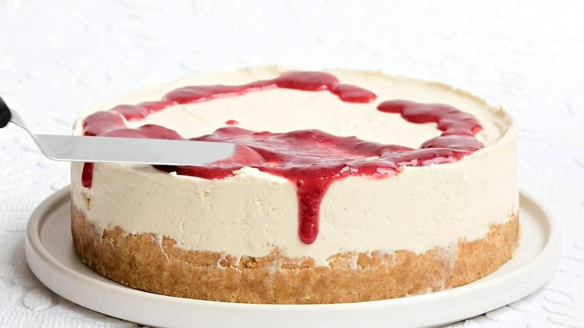 Spreading raspberry sauce over no bake white chocolate and raspberry Cheesecake