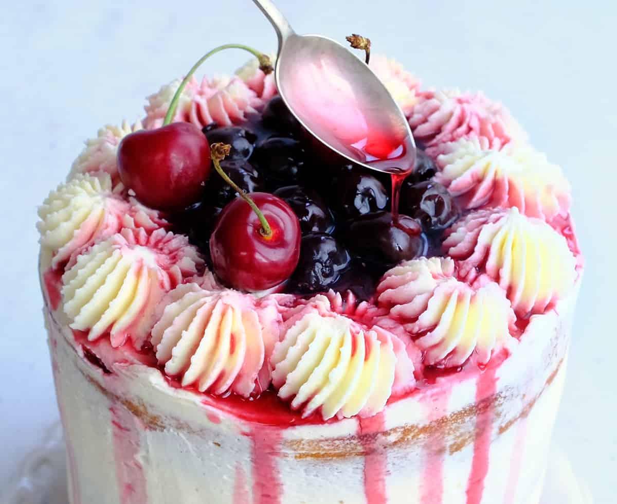 spooning cherry syrup over white forest cake