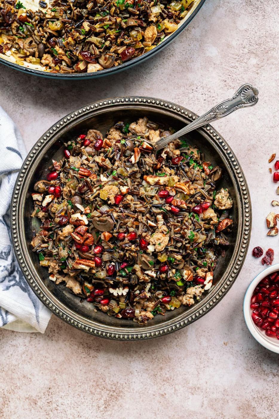 wild rice dressing with sausage in a bowl, chopped cranberries, pecans and pomegranate seeds on the side